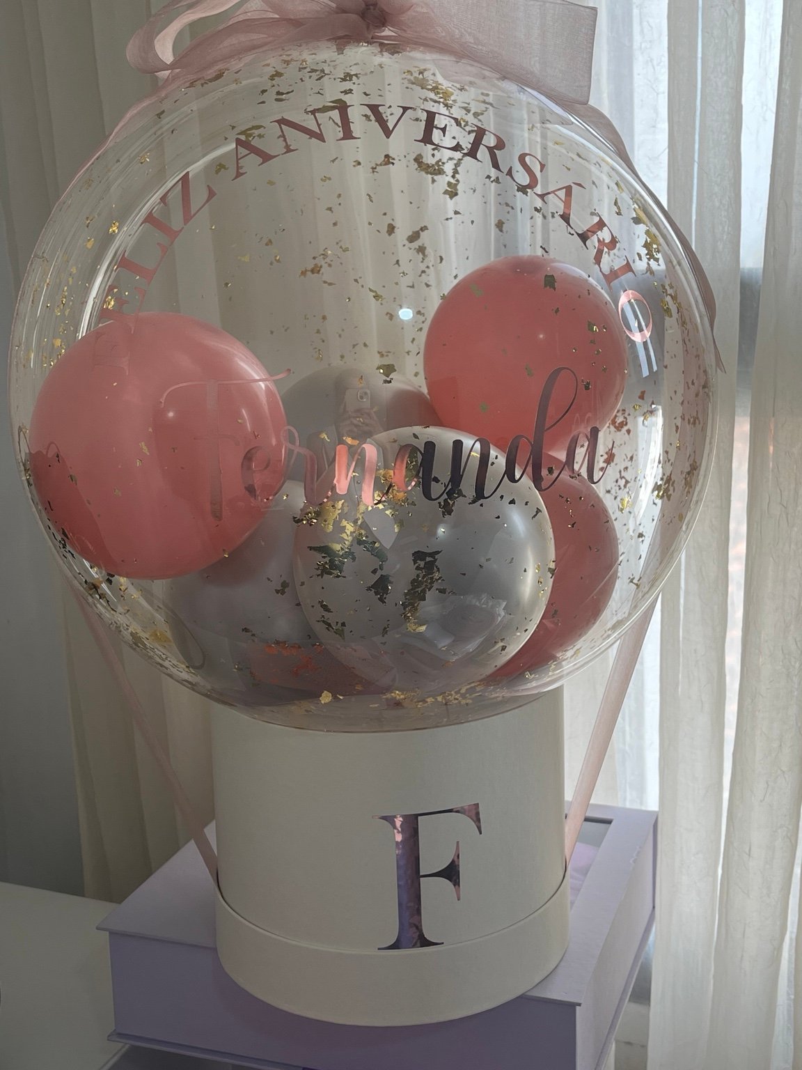 Balão transparente personalizado sobre caixa redonda com inicial